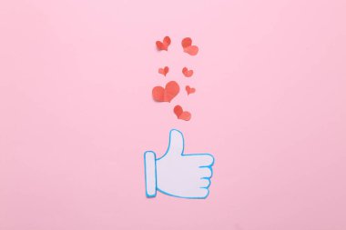 Kağıt kesiği, uyarı simgesini pembe arka planda kalpleri olan başparmağıyla kesiyor. Sosyal medya. Beğeni, takipçiler geri bildirim