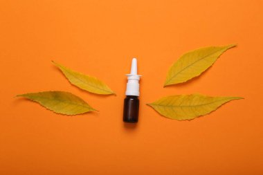 Sonbahar soğuğu tedavisi. Turuncu arka planda sarı yapraklı burun spreyi.