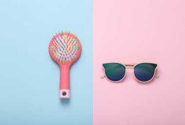 Kadın aksesuarları. Mavi-pembe arka planda saç fırçası olan güneş gözlüğü. Üst görünüm