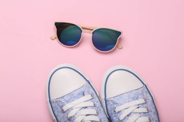 Pembe arka planda spor ayakkabıları ve güneş gözlüğü. Üst görünüm