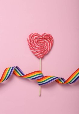 Eşitlik, lgbt topluluğu. Pembe arka planda gökkuşağı kurdelesi olan kalp şeklinde lolipop. Üst Manzara. Düz yatıyordu