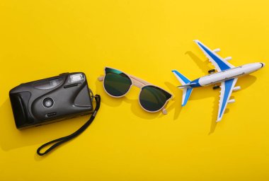 Seyahat konsepti. Parlak sarı arka planda güneş gözlüklü oyuncak uçak kamerası. Üst Manzara. Düz yatıyordu