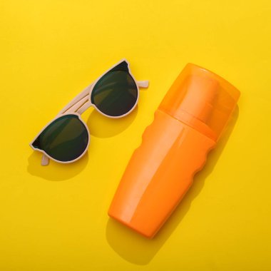Yaz zamanı. Tatil, sahil tatili, tatil konsepti. Sarı arka planda güneş gözlüğü ve bir şişe bronzlaştırıcı krem. Üst görünüm