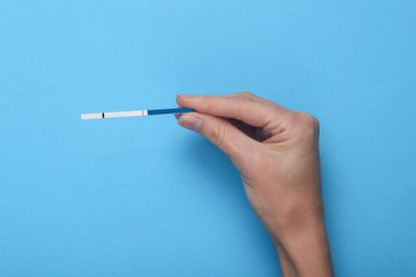 Mavi arka planda hamilelik testi tutan bir kadın.