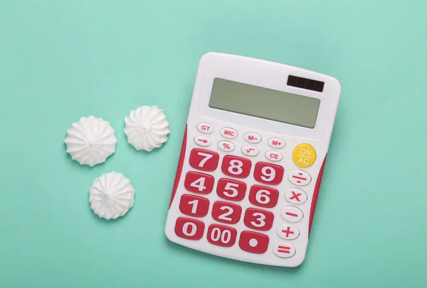 Calorie counting, diet concept. Sweet meringue with calculator on blue background. Top view. Flat lay
