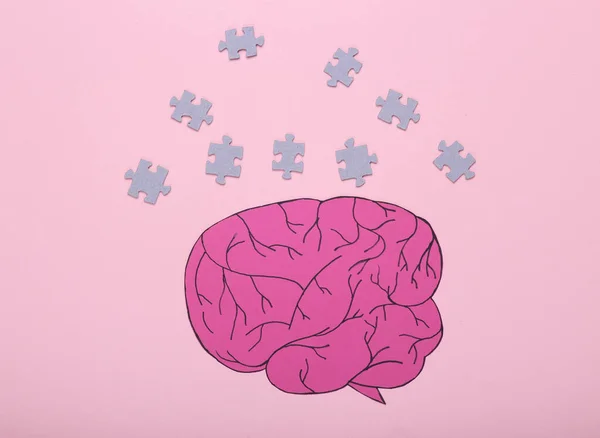 The concept of open consciousness, mental health, dementia. Paper cut brain with puzzle pieces on a pink background