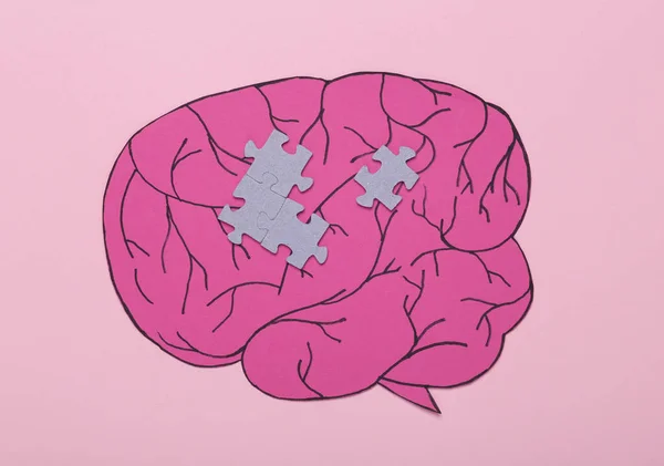 The concept of open consciousness, mental health, dementia. Paper cut brain with puzzle pieces on a pink background