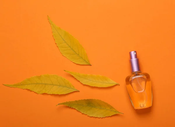 Perfume bottle with autumn leaves on orange background