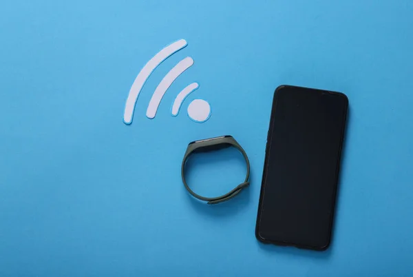 Paper cut Waves wi-fi icon with smart bracelet and smartphone on a blue background. Top view