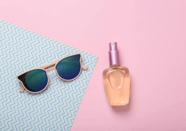 Women's accessories. Sunglasses with a bottle of perfume on a blue-pink pastel background. Top view