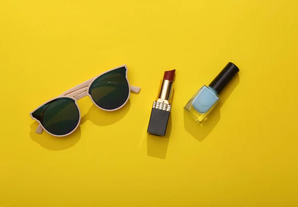 Cosmetics and accessories on a pink background. Sunglasses, nail polish and lipstick on bright yellow background. Top view