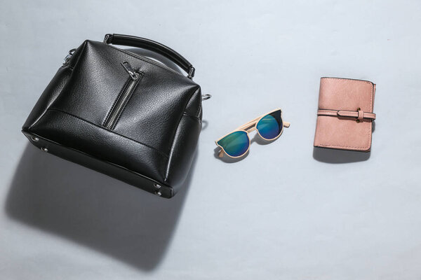 Стильные модные женские аксессуары на ярко-сером фоне с тенью. Бумажник, сумка и солнечные очки. Плоский лежал. Вид сверху