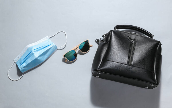 Медицинская маска в солнцезащитных очках и кожаная сумка на самом ярком фоне.