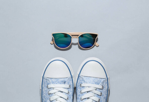 Sneakers with sunglasses on gray background. Top view. Flat lay
