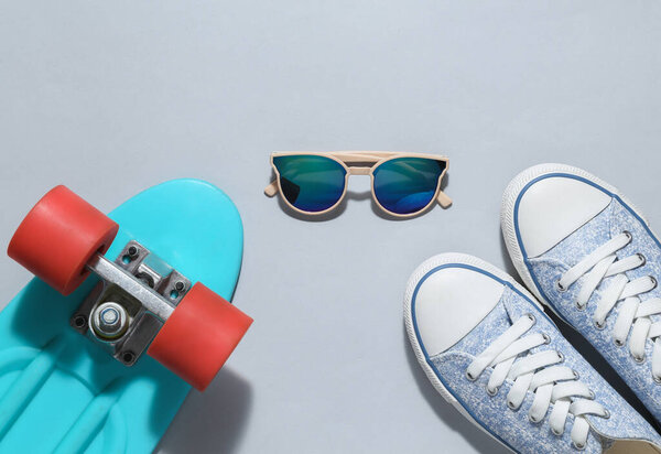 Hipster outfit on a gray background. Penny board with sunglasses and sneakers on a gray background. Top view. Flat lay