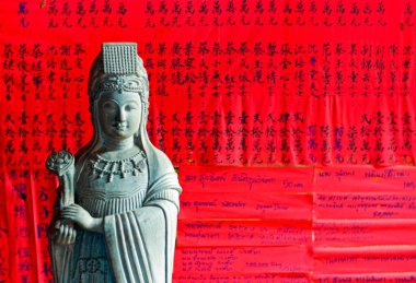 Hoi An, Vietnam - May 28, 2008: A statue in front of red sheets with writings of Buddhist prayers in a temple of the old town