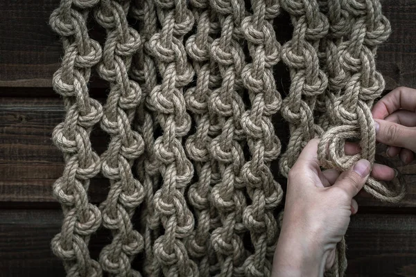 Bir kız büyük düğümlü dekoratif bir halı örüyor.