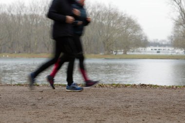 Parktaki çakıl yolunda koşan iki kişi var. Arka planda göl var.