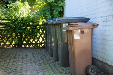 bir evin duvarına konmuş farklı çöp bidonları.