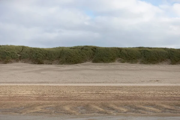 Kumsalda kum, arka planda çimen, bulutlu gökyüzü