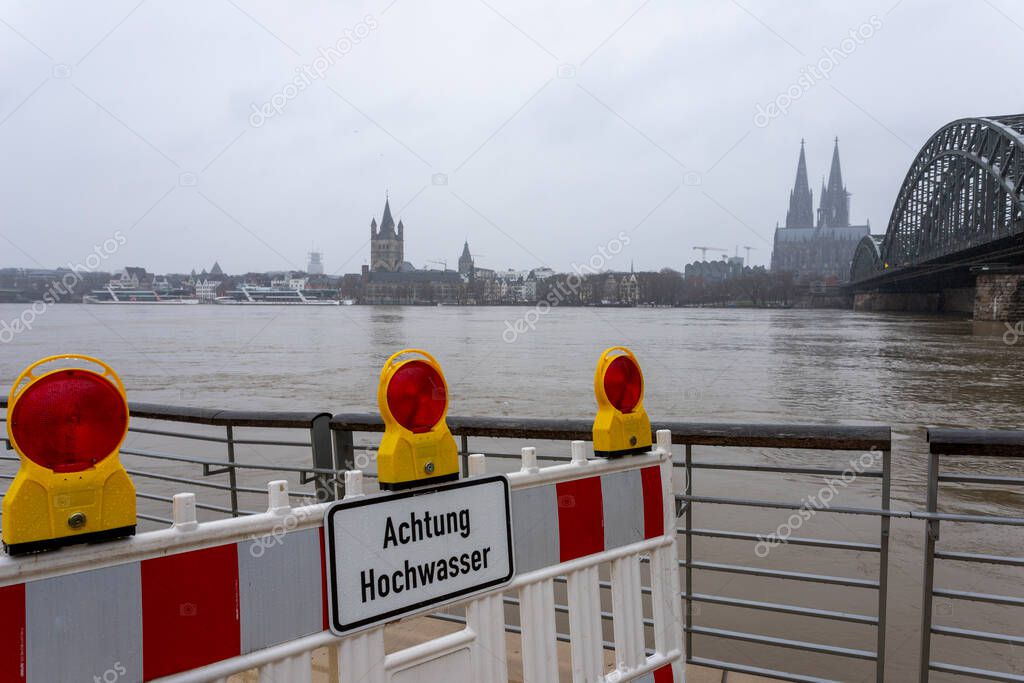 panorama of Cologne with cathedral and hohenzollern bridge at snowy weather. rhine river with high water, barrier with warning sign, german word for flood