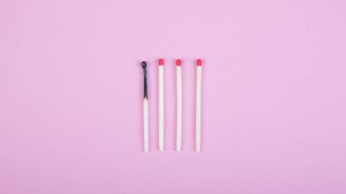 Dört kibrit çöpü, biri pembe arka planda yanmış.