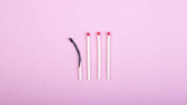 Dört kibrit çöpü, biri pembe arka planda yanmış.