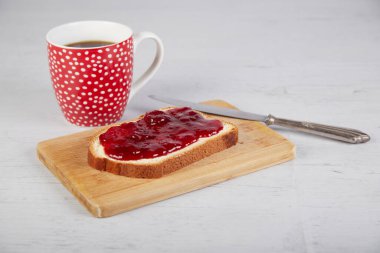 Kahve fincanı, çilek reçelli bir parça beyaz ekmek ve gümüş bir bıçak.