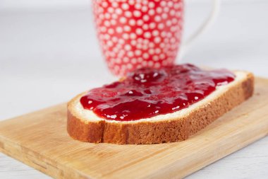 Kahve fincanı, çilek reçelli bir parça beyaz ekmek.