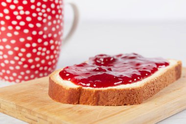 Kahve fincanı, çilek reçelli bir parça beyaz ekmek.