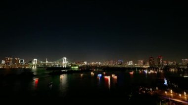Panoramic night cityscape, illuminated buildings, long bridge reflected in sea
