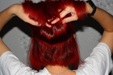 Genç kadın kırmızı boyalı parlak saçlar tutuyor. Bob kes. Arka görünüm.