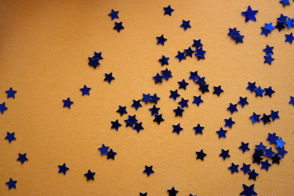 Blue stars glitter shiny confetti on a golden background. Christmas concept. Flat lay. Top view. Holiday template.