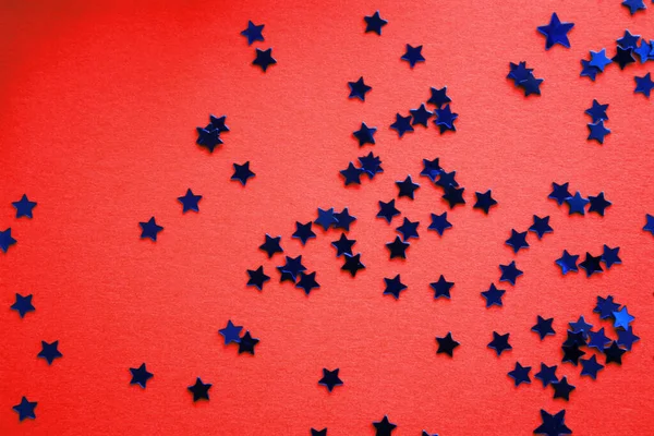 Blue stars glitter shiny confetti on a red background. Christmas concept. Flat lay. Top view. Holiday template.