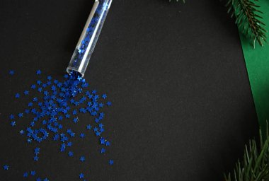 Siyah arka planda dağınık mavi yıldız konfetileri. Yeşil ladin dalları. Şablon şablonu. Dekoratif öğeler.