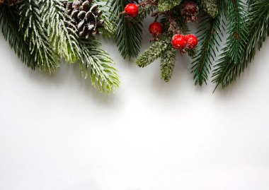 Noel tebrik kartı ladin dalları, canlı kırmızı böğürtlenler ve beyaz arka planda kar konileri ile süslenir. Yeni yıl kartpostalı. Üst görünüm.