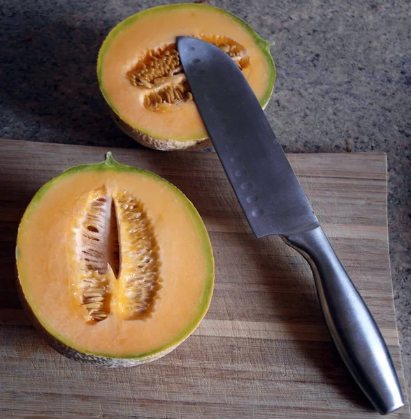 Halved honeydew melon with large knife on a cutting board