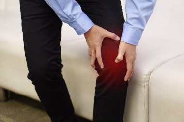 Resim, kanepede oturan işçilerin dizlerine acıdan ve yaradan dokunarak ellerini kullanmalarını gösteriyor. Sağlık ve Tıp Konsepti.