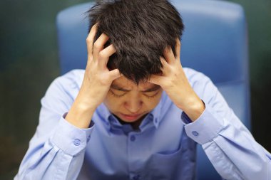 Ofiste mavi gömlek giyen Asyalı iş adamı, işten dolayı baş ağrısı çekiyor (yorgun, bitkin, zayıf). Sağlık ve Tıp Konsepti.