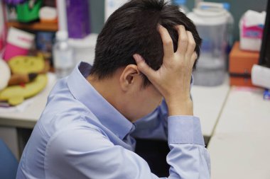 Ofiste mavi gömlek giyen Asyalı iş adamı, işten dolayı baş ağrısı çekiyor (yorgun, bitkin, zayıf). Sağlık ve Tıp Konsepti.