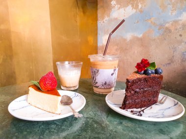 Coffee and dessert on the table in front of loft wall style, Cheesecake with strawberry, chocolate cake with blueberry