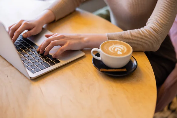 Vista Cortada Jovem Freelancer Usando Laptop Perto Xícara Cappuccino — Fotografia de Stock