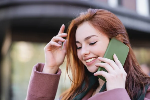 Mutlu kızıl saçlı kadın dışarıda akıllı telefondan konuşuyor. 