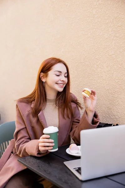 Cheerful Woman Holding Coffee Macaron Laptop Cafe Terrace — 스톡 사진