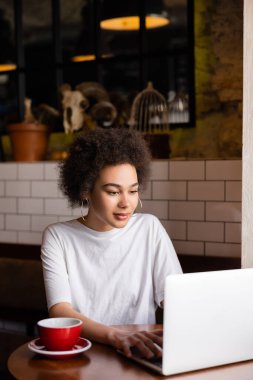 young african american woman using laptop near cup of coffee on table 