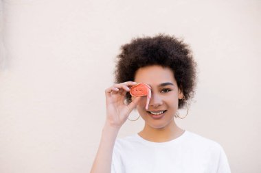 pleased young african american woman covering eye with jelly bubble tape on white