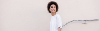 smiling young african american woman walking near rusty handrail, banner