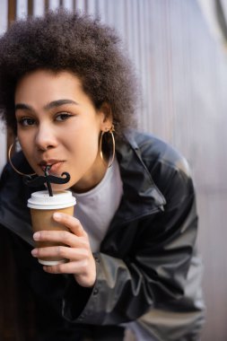 low angle view of young african american woman drinking takeaway beverage from straw with moustache