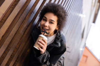 low angle view of cheerful african american woman drinking takeaway beverage from straw with moustache