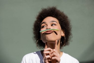 young african american woman holding jelly straw with mouth while grimacing outside